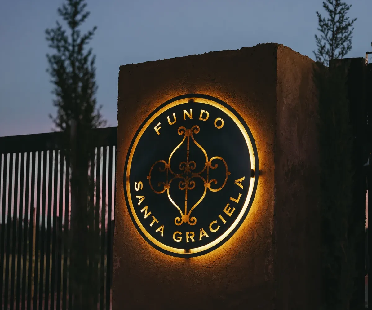Portal de acceso de Fundo Santa Graciela con el logotipo iluminado al anochecer